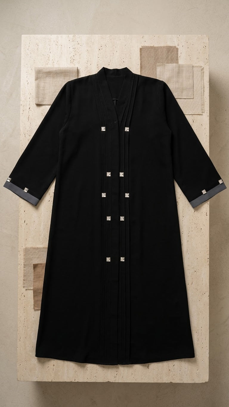 Black abaya with grey cuff detailing and square embellishments on a neutral textured backdrop