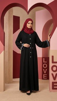 Black abaya with grey cuff detailing styled with a red hijab in an architectural setting